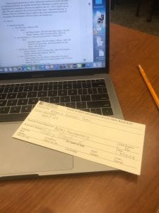 A slip of paper entitled Manuscript Division Collection Request sits on top of a macbook keyboard. Ashley Montgomery has filled the request out with her name, date 3/12/19, table number 36, and the following details: Box 1:102 from the William J. Brennan's Papers Collection.