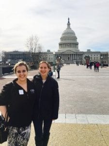 Megan and Natalie stand in front of the Capitol Building, far enough away so that you can see the full front exterior.