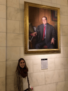 Natalia Albores standing underneath a large portrait of late Justice Antonin Scalia, painted by Nelson Shanks.