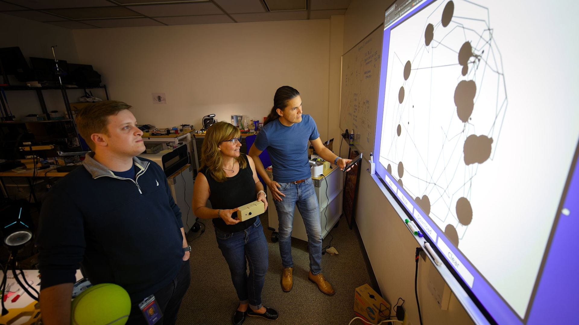 Three people reviewing a data visualization on a projected screen in a lab.
