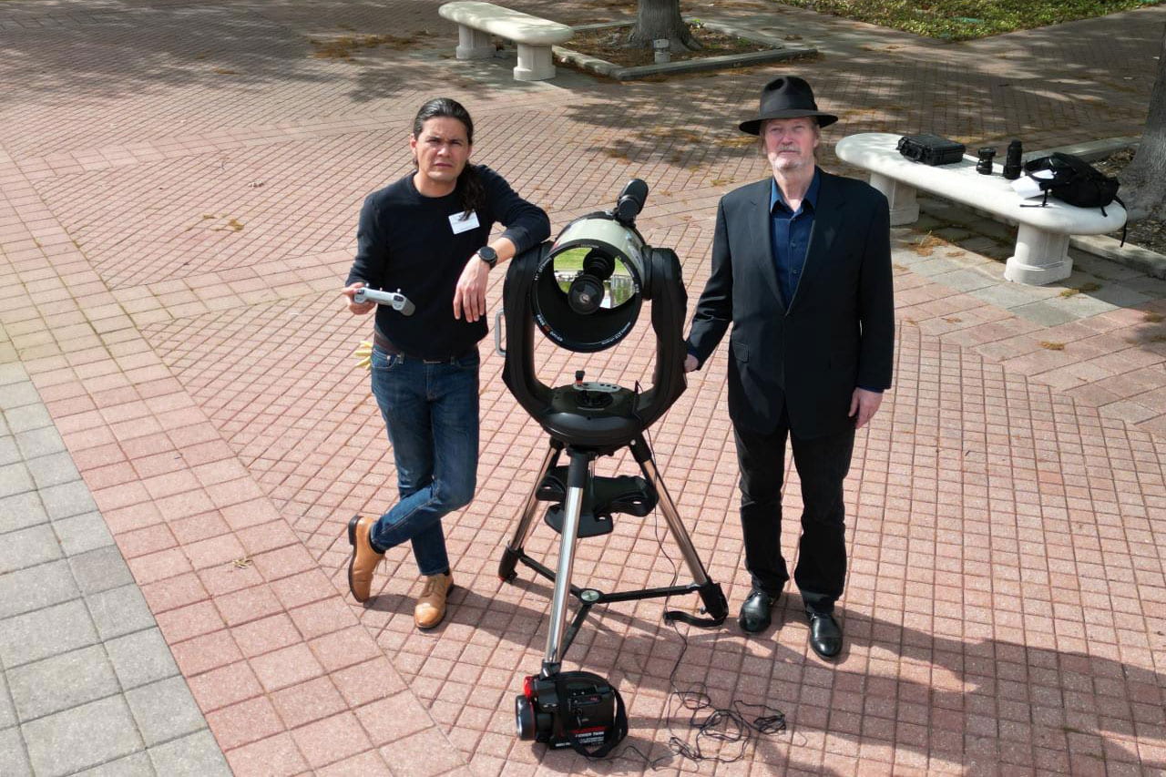 Two men standing outside with a large telescope.