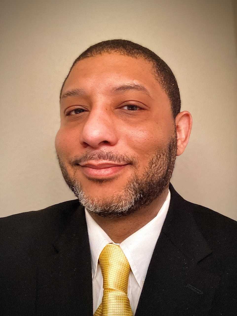 Photo of Rahni B. Kennedy; headshot black man in a suit with a gold tie