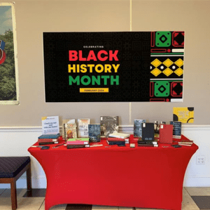 Table covered in red tablecloth and several books. Above the table is a large sign that says "Celebrating Black History Month."